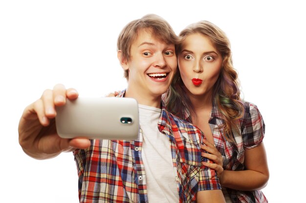Technologie-Liebes- und Freundschaftskonzept Lächelndes Paar mit Smartphone-Selfie und Spaß Studioaufnahme auf weißem Hintergrund