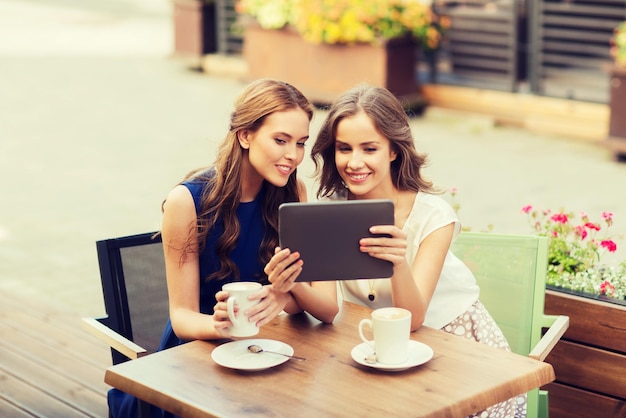 Technologie-, Lifestyle-, Freundschafts- und Menschenkonzept - glückliche junge Frauen oder Mädchen im Teenageralter mit Tablet-PC-Computer, die Kaffee im Café im Freien trinken
