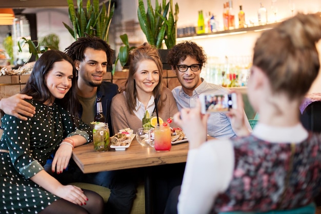 Technologie-, Lifestyle- und Menschenkonzept - glückliche Freunde mit Smartphone-Fotografieren in Bar oder Café