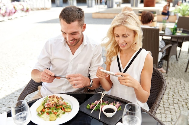 Technologie, Menschen, Essen und Freizeitkonzept - glückliches Paar mit Smartphone, das Essen auf der Restaurantterrasse fotografiert