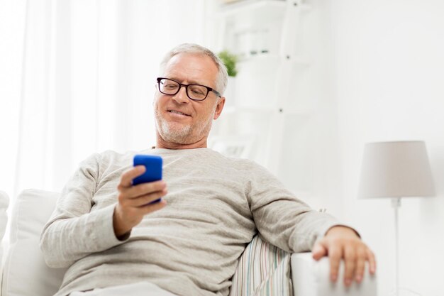 Technologie, Menschen, Lifestyle und Kommunikationskonzept - glücklicher älterer Mann, der die Telefonnummer wählt und zu Hause auf dem Smartphone SMS schreibt