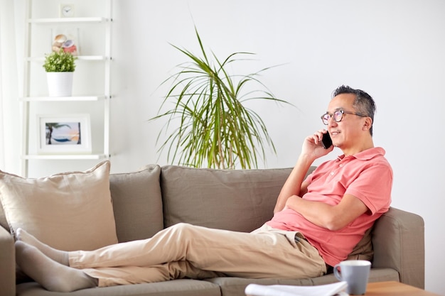 Technologie, Menschen, Lifestyle und Kommunikationskonzept – glücklicher Mann sitzt auf dem Sofa und telefoniert zu Hause mit dem Smartphone