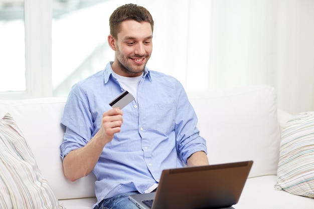 Technologie, Menschen und Online-Shopping-Konzept - lächelnder Mann mit Laptop und Kreditkarte zu Hause