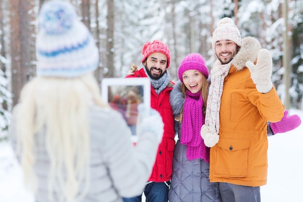 Technologie-, Saison-, Freundschafts- und Personenkonzept - Gruppe lächelnder Männer und Frauen, die mit einem Tablet-PC-Computer im Winterwald fotografieren