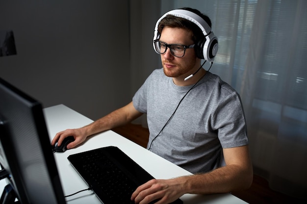 Technologie, Spiele, Unterhaltung, Let's Play und People-Konzept - junger Mann mit Headset und Brille mit PC-Computer, der zu Hause ein Spiel spielt und Playthrough oder Walkthrough-Video streamt