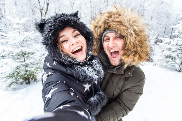 Technologie- und Beziehungskonzept - Glückliches lächelndes Paar, das ein Selfie in einem Winterwald nimmt