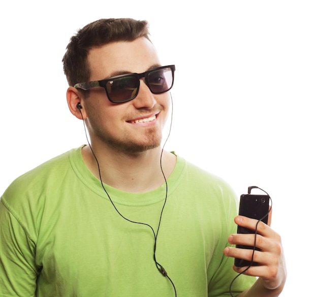 Technologie- und Personenkonzept Junger Mann mit grünem T-Shirt, der Musik hört und Smartphone isoliert auf Weiß verwendet