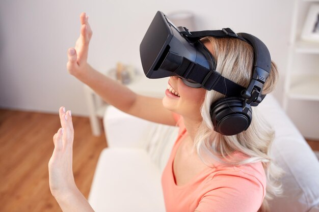 technologie, virtuelle realität, unterhaltung und menschenkonzept - glückliche junge frau in virtual-reality-headset oder 3d-brille und kopfhörern, die zu hause ein spiel spielen und etwas unsichtbares berühren