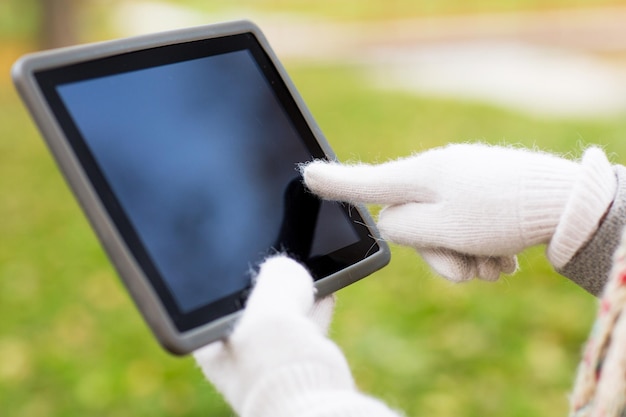 Technologie-, Werbe- und Personenkonzept - Nahaufnahme von Händen in Herbsthandschuhen, die Tablet-PC-Computer mit schwarzem, leerem Bildschirm im Freien halten