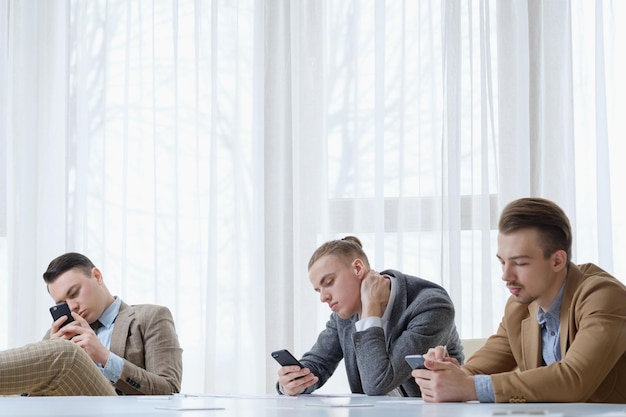 Technologieabhängige Geschäftsleute, die ihre Telefone im Büro benutzen, treffen sich im Leerlauf und Arbeitsstil