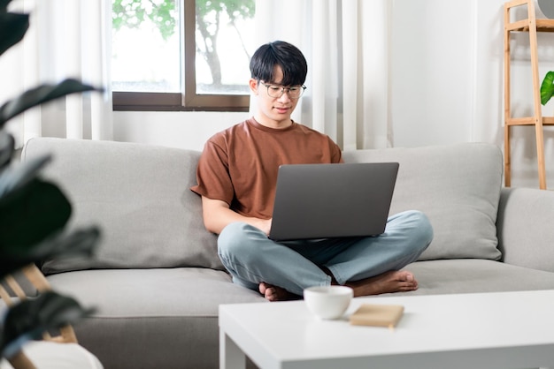 Technologiekonzept Der Mann sitzt auf dem Sofa, ruht sein Notebook auf seinem Schoß und erledigt seine Arbeit