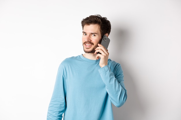 Technologiekonzept. Junges männliches Model telefoniert mit dem Handy, ruft jemanden auf dem Smartphone an und lächelt, steht auf weißem Hintergrund