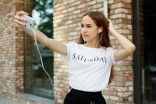 Foto technologien, emotionen, menschen, beauty, mode und lifestyle-konzept - unbeschwerte und fröhliche, sonnige frühlingsstimmung. charmante junge dame macht selfie auf einer kamera. bei einem stadtspaziergang im freien