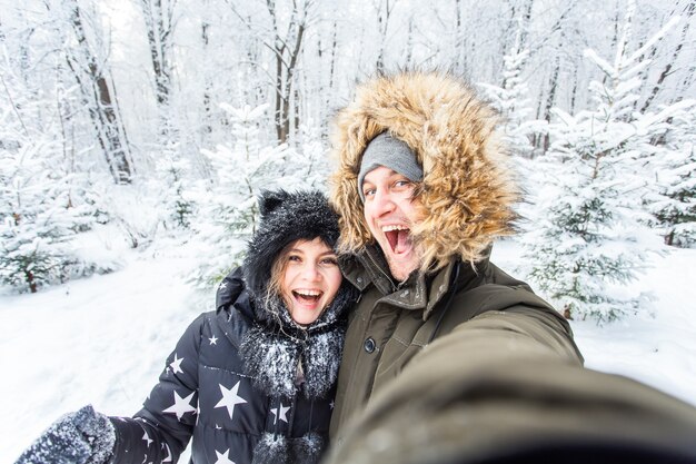 Technologien und Beziehungskonzept - Glückliches lächelndes Paar, das draußen ein Selfie in einem Winterwald macht.