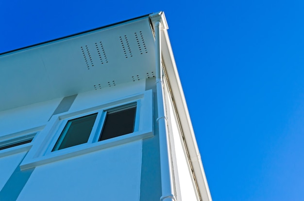 Techo de la casa con canalón de lluvia de la casa en la azotea y grandes ventanales sobre fondo de cielo azul Nuevo moderno