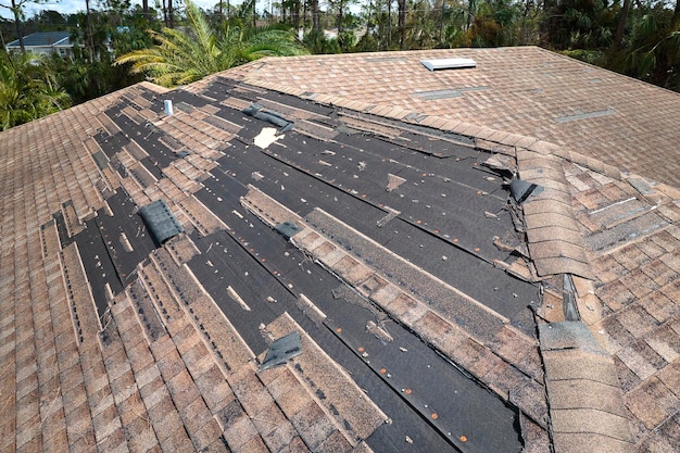 Techo de casa dañado por el viento con tejas de asfalto faltantes después del huracán Ian en Florida Reparación del concepto de techo de casa