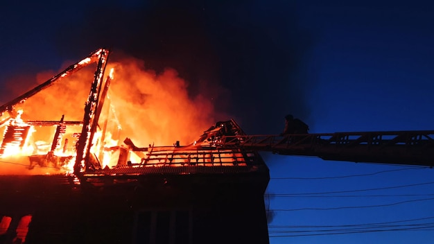 El techo de la casa está en llamas. El edificio residencial quema el pueblo. Los bomberos apagan un incendio desde la grúa desde arriba. El departamento de bomberos apaga la llama abierta. Humo y chispas.