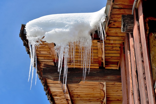 Techo de casa de madera en pueblo alpino cubierto de nieve y carámbanos