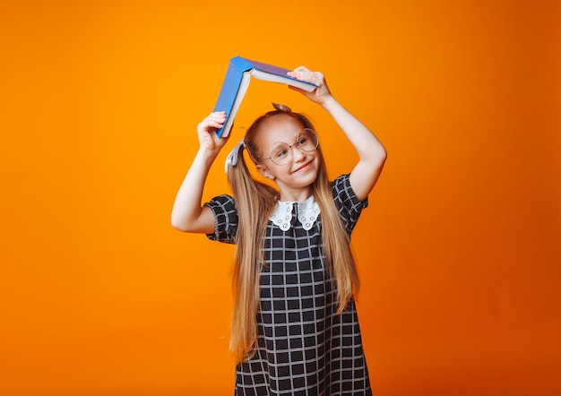 Un techo de libros sobre tu cabeza Una niña pequeña sostiene un libro de texto sobre su cabeza Una niña pequeña con un libro sobre un fondo naranja