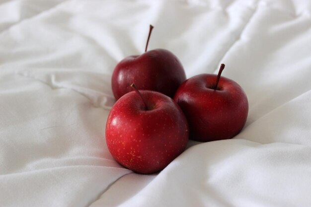 Tecido branco e três maçãs vermelhas inteiras nele Foto detalhada