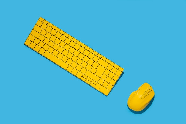 Teclado amarillo y mouse de computadora amarillo sobre un fondo azul Vista superior plana