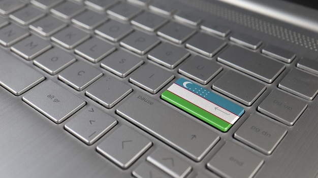 Foto el teclado con la bandera de uzbekistán en el botón de entrada representa el lenguaje de aprendizaje del ataque cibernético