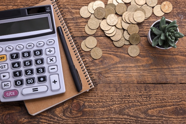 Teclado de la calculadora, monedas de oro, bolígrafo y cuaderno sobre un fondo de piso de madera. Vista superior. Copie el espacio.