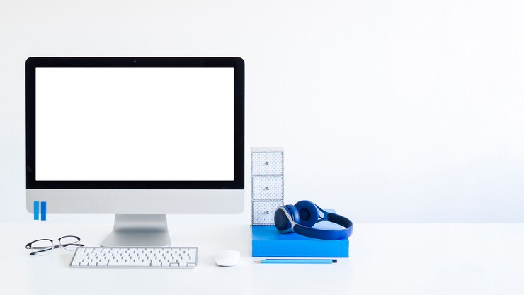 Foto teclado cerca del monitor, ratón de la computadora, lentes y auriculares en la mesa