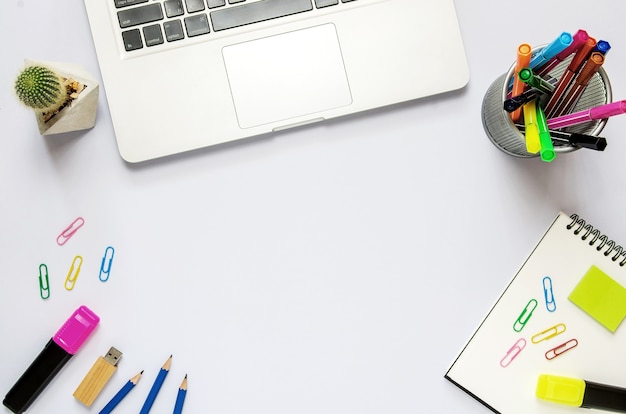 Teclado de computadora con bloc de notas, cactus, clip, lápiz, pendrive, marcador de color pluma en el escritorio blanco.