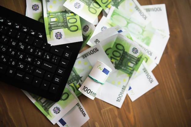 Teclado de computadora y una dispersión de billetes de 100 euros sobre la mesa El trabajo de un programador y blogger en Internet