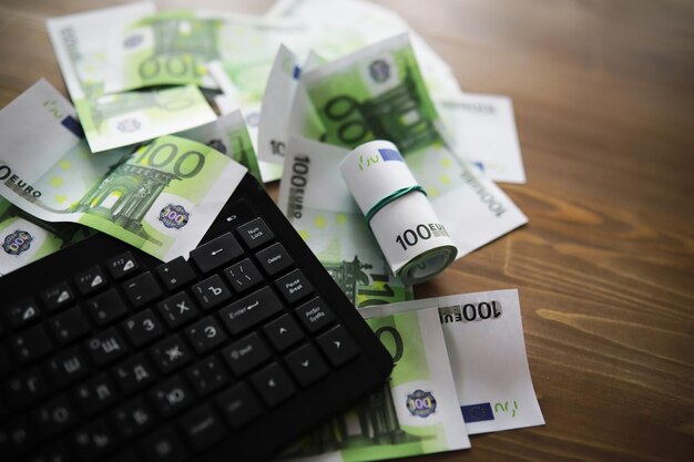 Teclado de computadora y una dispersión de billetes de 100 euros sobre la mesa El trabajo de un programador y blogger en Internet