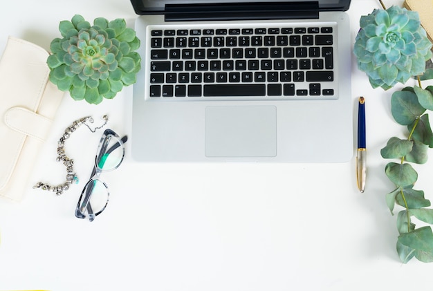 El teclado de la computadora portátil con accesorios de mujer dorada y plantas verdes simulan una escena de estilo plano