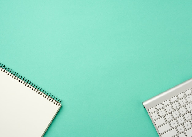 Foto teclado de alumínio sem fio branco e notebook aberto com lençóis brancos em branco sobre um fundo verde