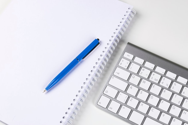 Teclado de computador sem fio, caderno e caneta na mesa do escritório comercial