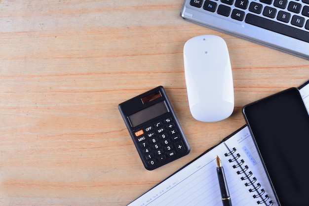 Teclado e mouse, caneta-tinteiro, caderno, calculadora e smartphone em uma mesa