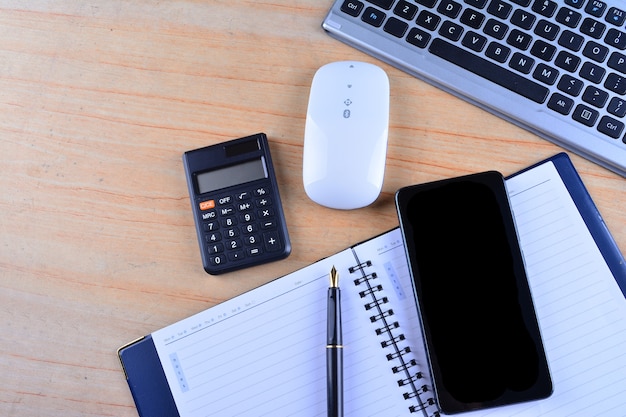 El teclado con mouse, pluma estilográfica, cuaderno, calculadora y teléfono inteligente sobre una mesa