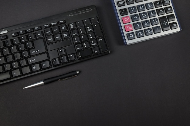 Teclado negro con calculadora y bolígrafo sobre fondo negro Vista superior Copiar espacio