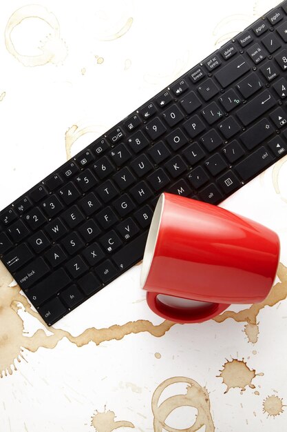 Foto un teclado de portátil derramado y una taza roja de café volcada sobre un fondo blanco con manchas de café