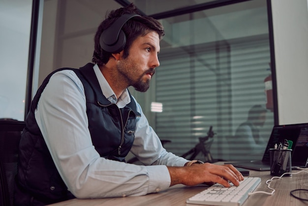 Teclado de programador de auriculares y hombre que escribe codificación o programación en línea por la noche Computadora de tecnología de la información y empleado masculino o codificador que trabaja en software mientras transmite música o radio