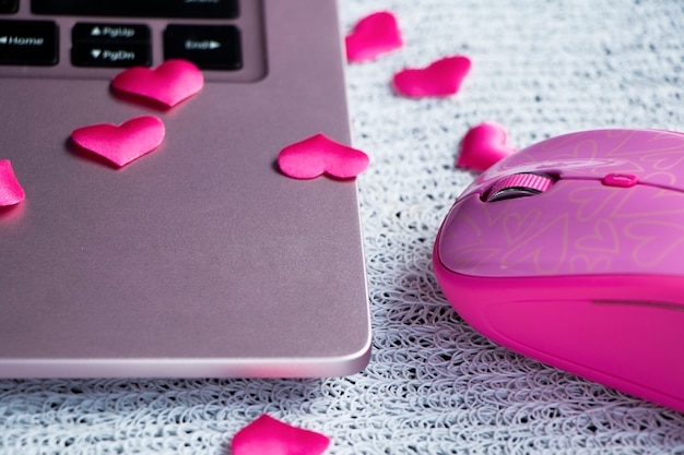 Teclado rosa para portátil Ratón rosa para portátil sobre una mesa de luz con corazones dispersos encontrando el amor en línea