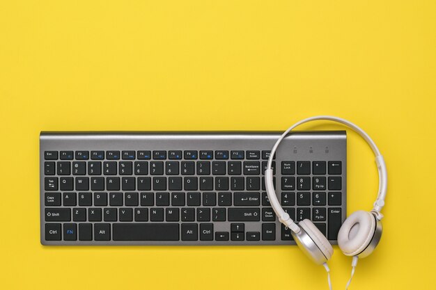 Foto teclado sem fio e fones de ouvido brancos em uma mesa amarela. dispositivos periféricos para o computador. a vista do topo.