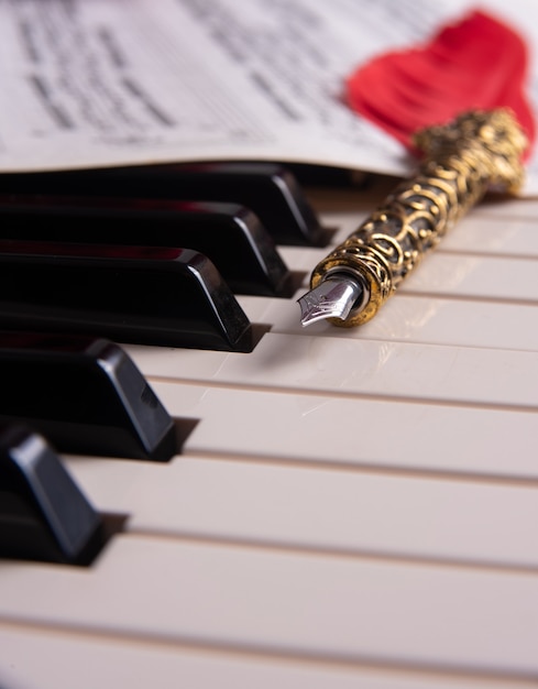 Foto teclas de un piano, pluma estilográfica y partitura musical, enfoque selectivo.