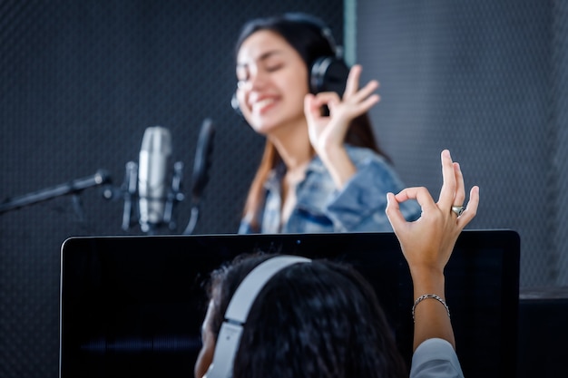 Técnica de estúdio feminina do monitor do computador de software para gravação em primeiro plano de jovem vocalista asiática usando fones de ouvido gravando uma música na frente do microfone em um estúdio profissional