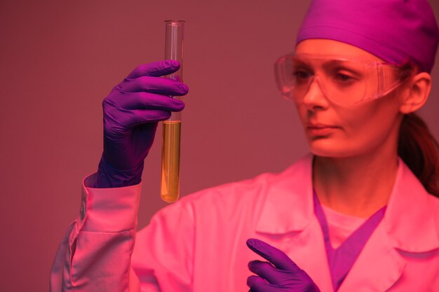 Foto técnica de laboratório séria usando luvas segurando um longo tubo de ensaio cheio de urina enquanto faz a análise