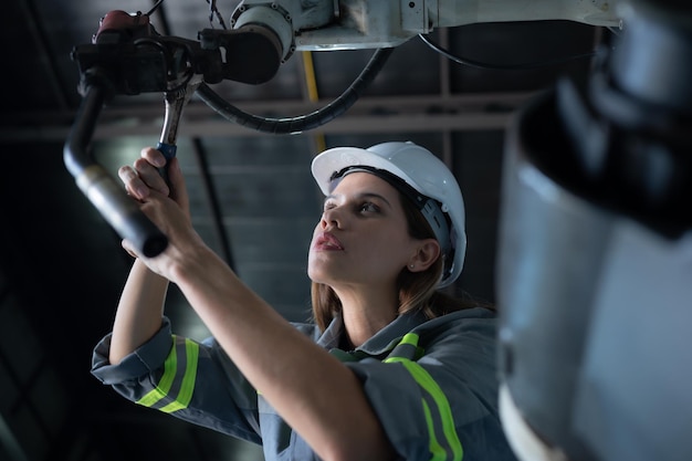 Foto técnica femenina inspeccionar y reparar el brazo robótico en el hangar de robots y probar el funcionamiento de la máquina después de ser utilizada durante un tiempo, además de actualizar el software y la calibración