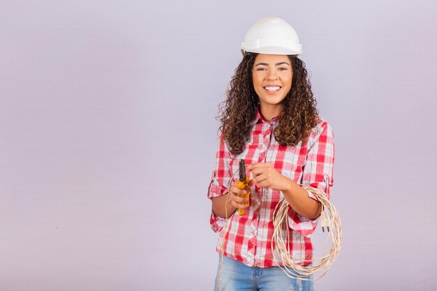 Técnica feminina. Mulher eletricista em fundo branco, com espaço para texto. Eletricista de mulher segurando o fio e um alicate.