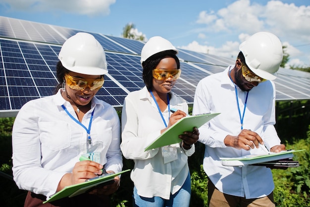 Técnico americano africano verifica a manutenção dos painéis solares Grupo de três engenheiros negros reunidos na estação solar