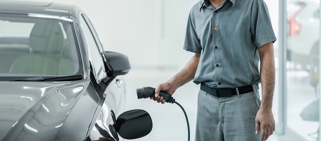 Técnico asiático senior está cargando el automóvil eléctrico o EV en el centro de servicio para su mantenimiento, concepto de energía alternativa ecológica