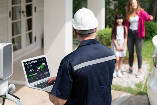 Técnico calificado que trabaja en la instalación de la estación de carga de vehículos eléctricos en el hogar, solucionando problemas y configurando el sistema de carga con una computadora portátil para vehículos eléctricos en casa con la familia presente Synchronos