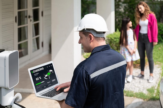 Técnico calificado que trabaja en la instalación de la estación de carga de vehículos eléctricos en el hogar, solucionando problemas y configurando el sistema de carga con una computadora portátil para vehículos eléctricos en casa con la familia presente Synchronos